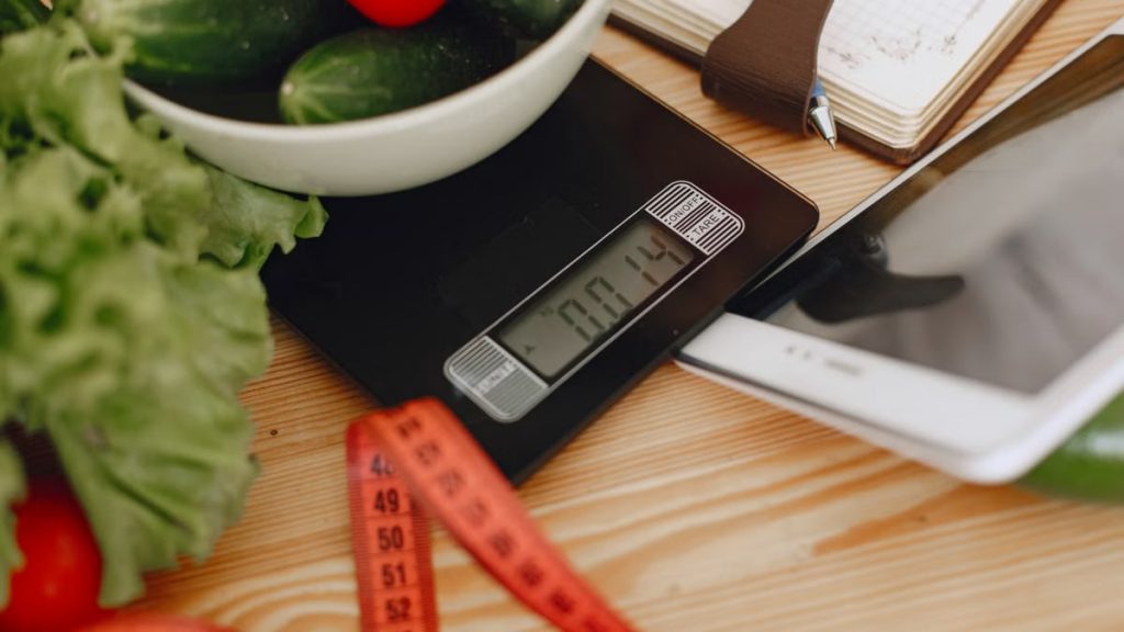 A bowl of fresh vegetables on a kitchen scale with measurement tools, depicting a healthy lifestyle.