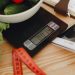 A bowl of fresh vegetables on a kitchen scale with measurement tools, depicting a healthy lifestyle.