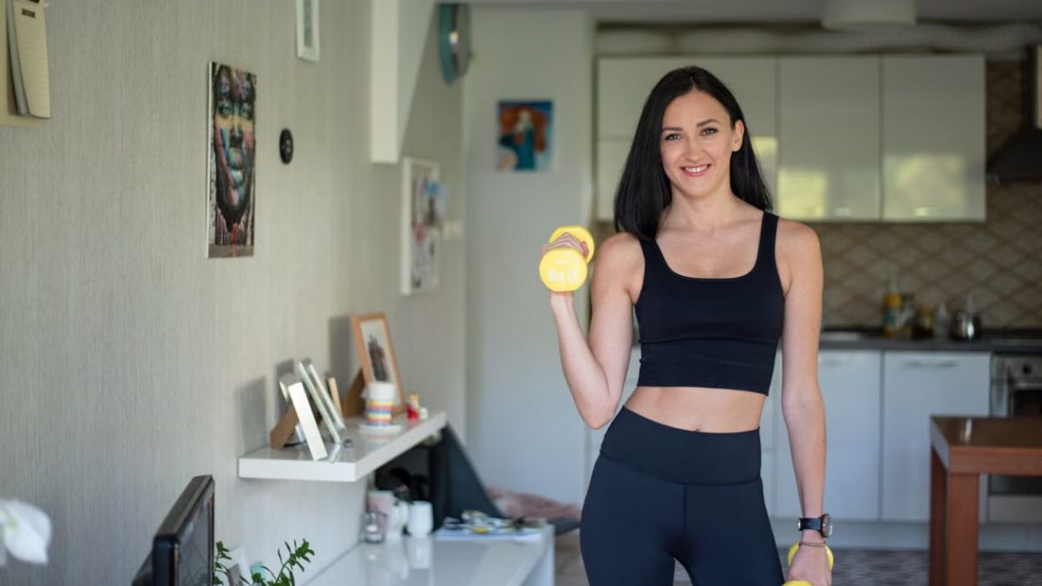 Smiling woman in activewear lifting dumbbells at home for a healthy lifestyle.