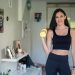 Smiling woman in activewear lifting dumbbells at home for a healthy lifestyle.